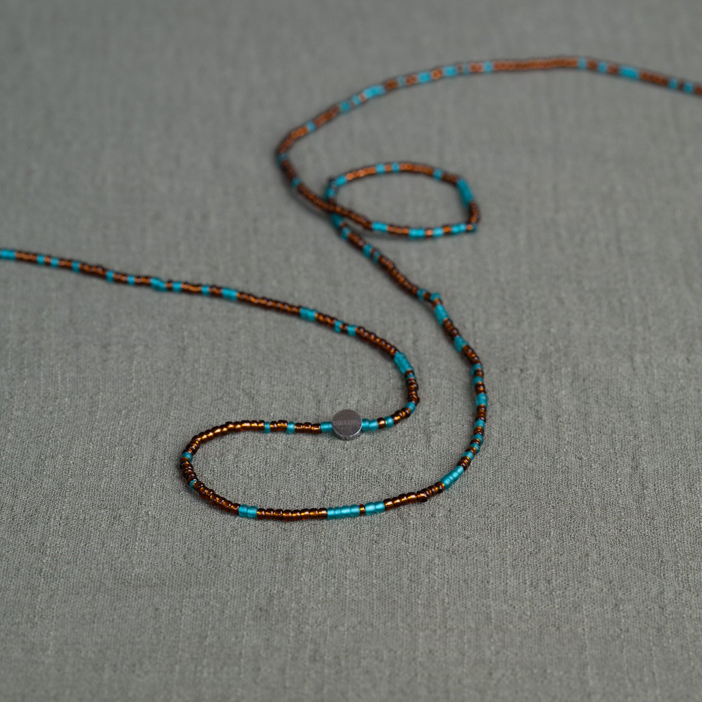 Earth-toned Ghanaian waist beads in turquoise and bronze – traditional African body jewelry representing rooted femininity.