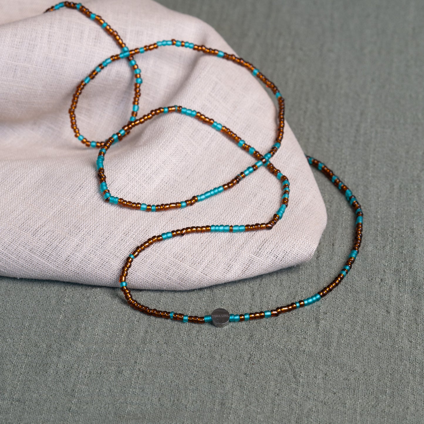 Earth-toned Ghanaian waist beads in turquoise and bronze – traditional African body jewelry representing rooted femininity.