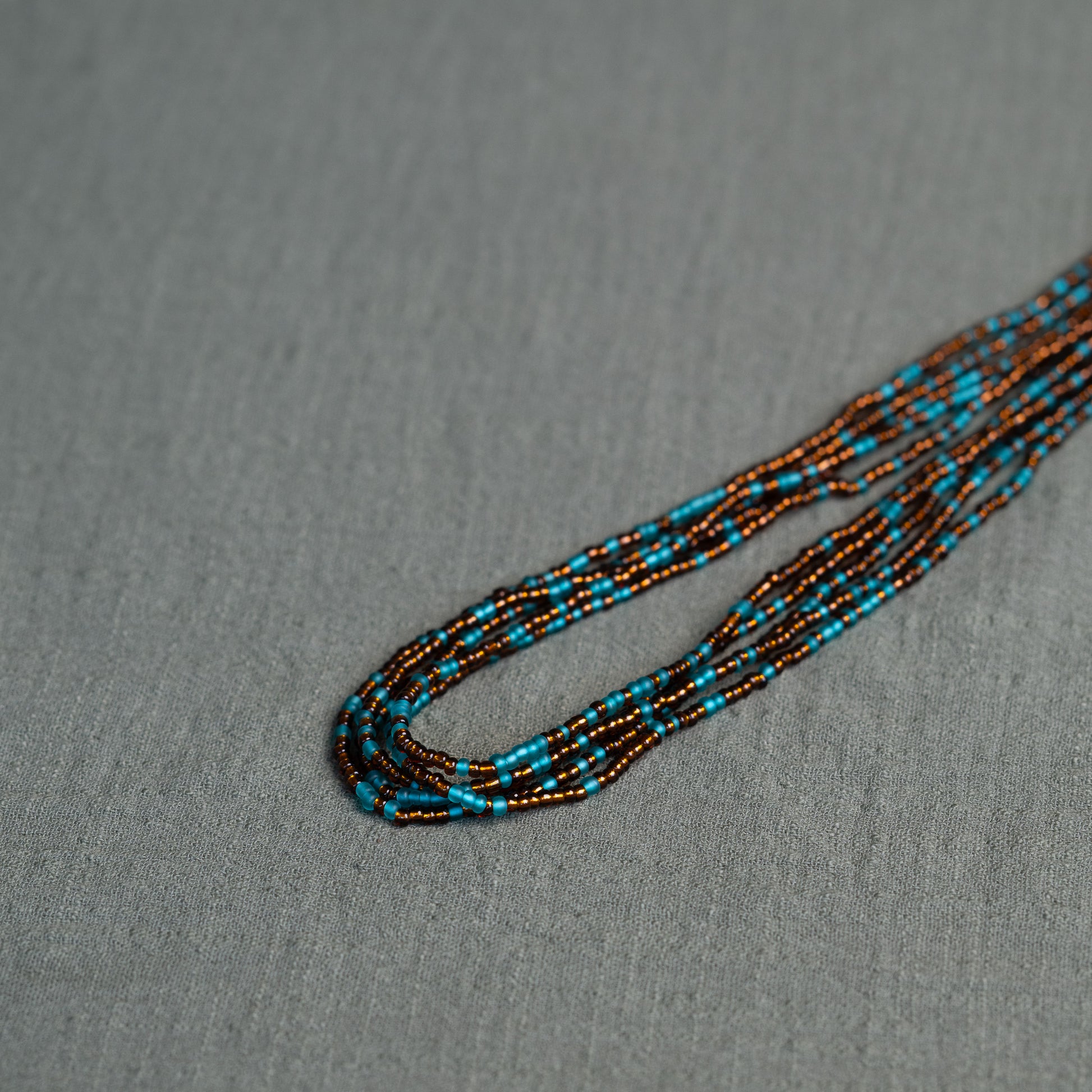 Earth-toned Ghanaian waist beads in turquoise and bronze – traditional African body jewelry representing rooted femininity.